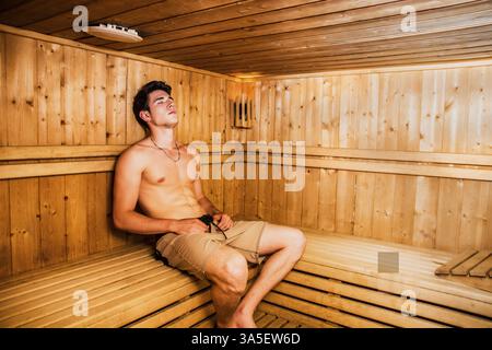 Young Handsome Muscular Man Relaxing in Sauna, Sitting on Wooden Bench Stock Photo