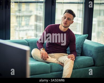 Young man sitting watching television changing the channel with the remote control Stock Photo