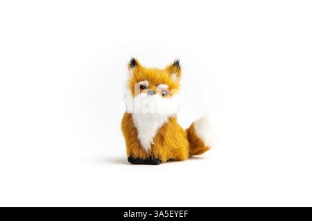 A small, plush fox toy sits against a white background. It has orange and white fur and a black nose. Stock Photo
