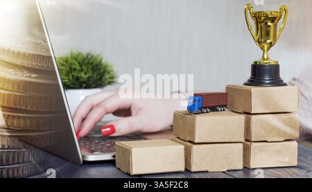 Stacks of cardboard boxes with money on top, next to a laptop displaying stock market candlestick charts, symbolizing financial investment and growth. Stock Photo