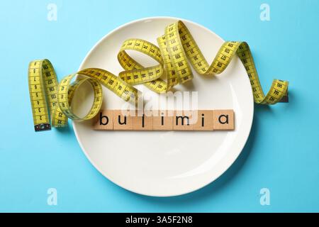 Plate with word Bulimia and measuring tape on light blue background, top view Stock Photo