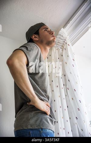 Young handsome man or handyman installing curtains over window at home, doing renovation work Stock Photo