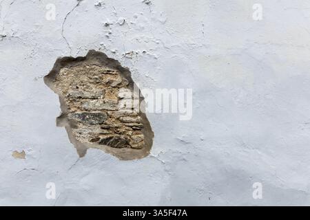 Front view white plastered wall with damaged part, original stones visible for​ vintage​ background. Stock Photo