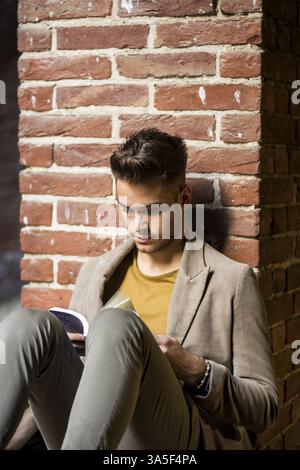 Male student reading book outdoor. Handsome young man reads a book sitting outside Stock Photo