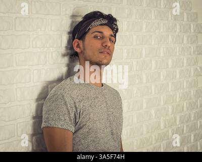 Handsome young man bandanna leaning on wall, looking at camera seductively Stock Photo