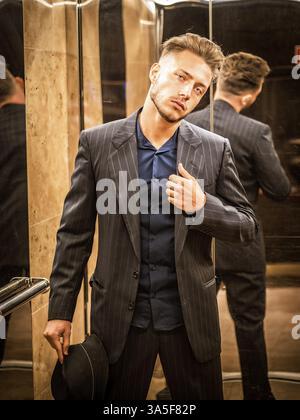 Handsome young business man leaning against mirror inside an elevator or lift, looking at camera Stock Photo