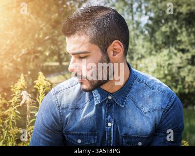 Handsome young man at countryside, in front of field or grassland, wearing shirt, looking away to a side Stock Photo