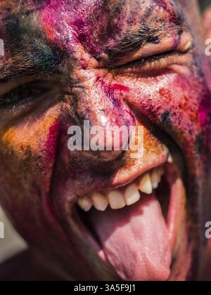 A close up of a painted man with his mouth open, doing silly face with tongue sticking out and one eye winking Stock Photo