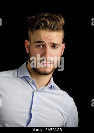 Handsome young man portrait with doubtful, unsure expression, isolated on black background Stock Photo