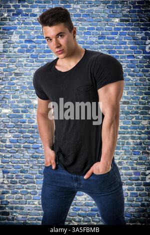Handsome young muscular man looking at camera shot over blue bricks wall background Stock Photo