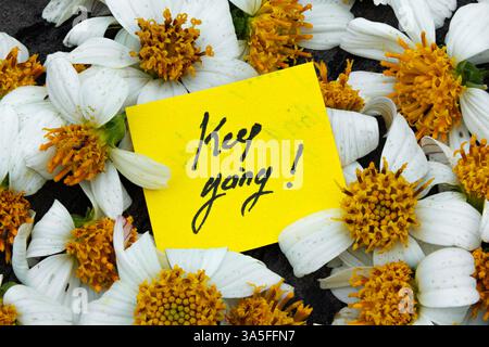 Motivational Message on Yellow Sticky Note with Flowers. Keep Going! Inspirational Note with White Wildflowers Stock Photo