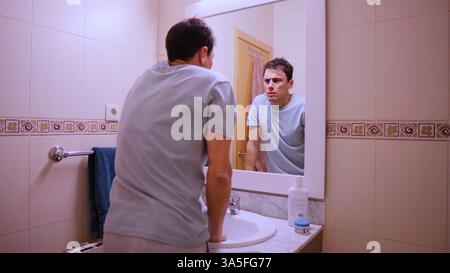 Sleepy man looking at his reflection in the bathroom mirror on monday morning Stock Photo