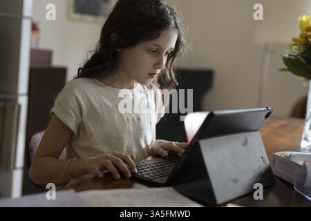 Girl, 10 years old, sits at the table with a tablet and learns Stock Photo