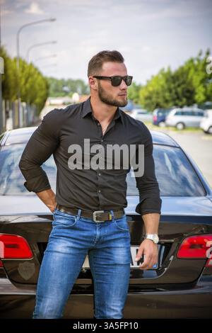 Portrait of young bearded man in sunglasses leaning on his new stylish polished car outdoor Stock Photo