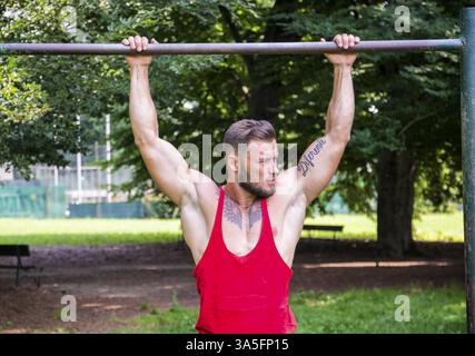 Muscular man hanging on bar and performing calisthenics pull up ...
