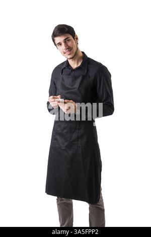 Young chef or waiter posing, wearing black apron and shirt isolated on white background, taking order writing on handheld device Stock Photo