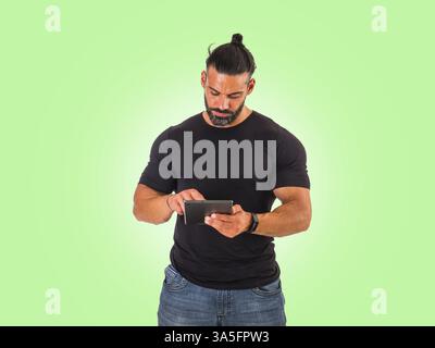 Attractive muscular man using electronic tablet, tapping on it, standing in studio shot Stock Photo