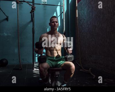 Handsome muscular young man exercising biceps in gym with dumbbells Stock Photo