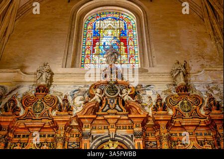 Low-angle view of a stone altar with a stained glass window in the background, interior features in the Seville Cathedral. Stock Photo