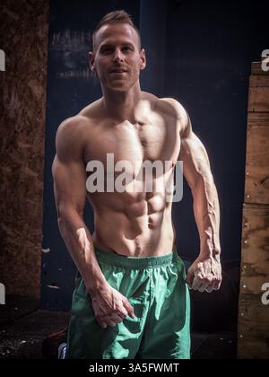 Handsome muscular young man standing in gym during workout, looking at camera Stock Photo