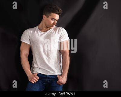 Handsome young muscular man looking down to a side, in studio shot over neutral dark background Stock Photo