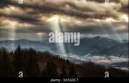 Sun rays shining through dark clouds on the hills Stock Photo