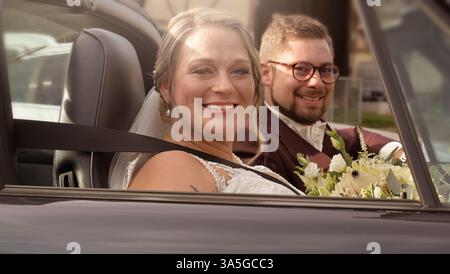 Bride and groom, couple in Cabrio car on wedding day. Portrait of a wedding couple bride and groom on their wedding day, the couple embrace. Stock Photo