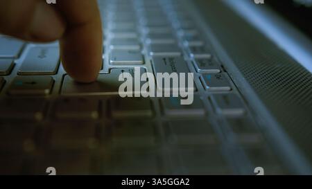 Close-up of a Finger Pressing the Enter Key on a Laptop Keyboard in a Dark Room Stock Photo