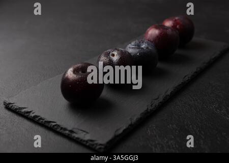 Juicy ripe fresh plum with water drops on black slate board. Seasonal fruit on black background. Selective focus, close-up. Stock Photo