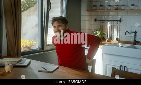 Man Experiencing Back Pain While Sitting in a Cozy Kitchen Stock Photo