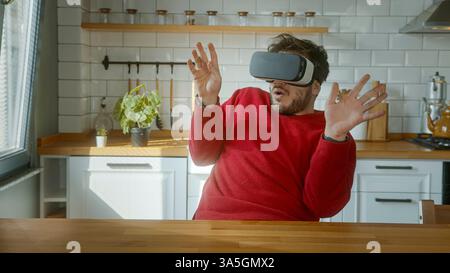Man Engaged in Virtual Reality Experience, Reacting with Fear and Surprise in a Modern Home Kitchen Stock Photo