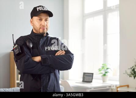 Portrait of confident male police officer standing in office wearing uniform with walkie talkie Stock Photo