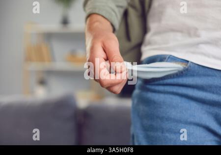 Poor man turning inside and showing empty pocket with no money standing in living room at home Stock Photo