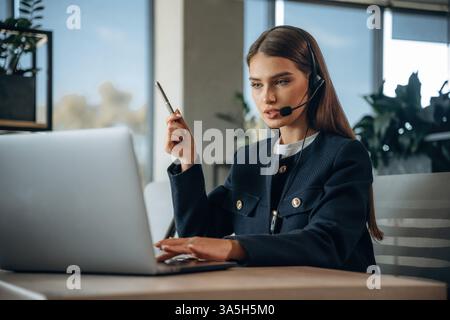 Advice, using laptop and headphones, talking. Woman is working in the office. Stock Photo