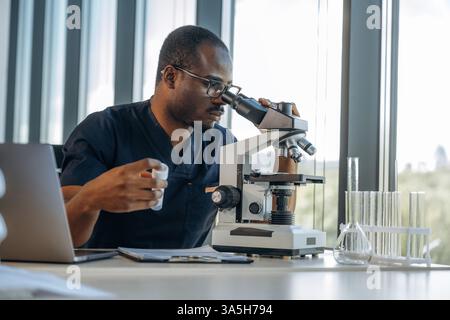 Test tube in hand, using the microscope. Scientist is working indoors. Stock Photo