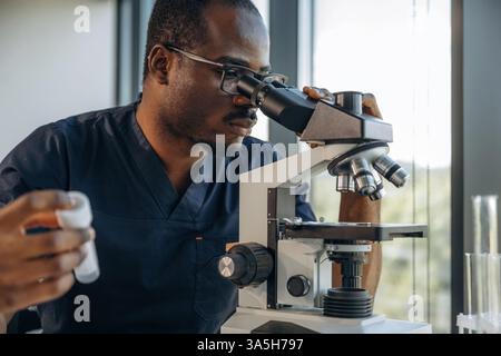 Test tube in hand, using the microscope. Scientist is working indoors. Stock Photo
