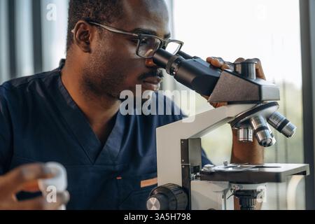 Test tube in hand, using the microscope. Scientist is working indoors. Stock Photo