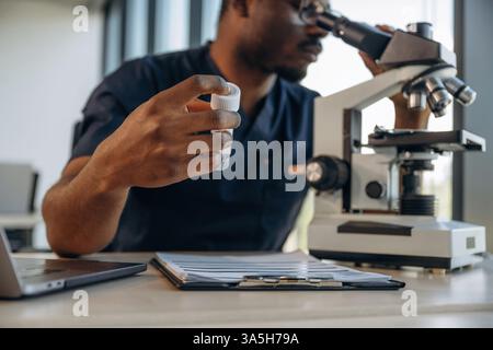 Test tube in hand, using the microscope. Scientist is working indoors. Stock Photo