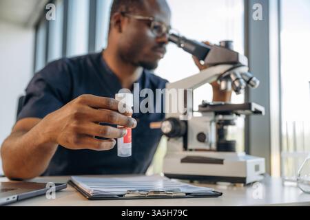 Test tube in hand, using the microscope. Scientist is working indoors. Stock Photo