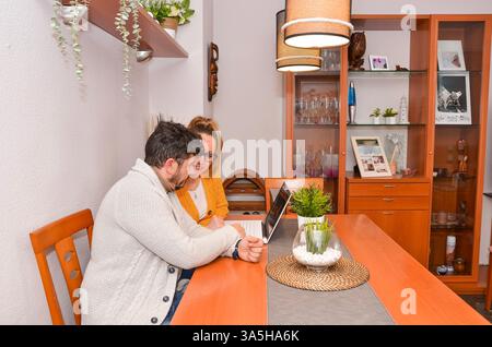 Couple sitting at dining table using laptop, browsing internet and smiling Stock Photo