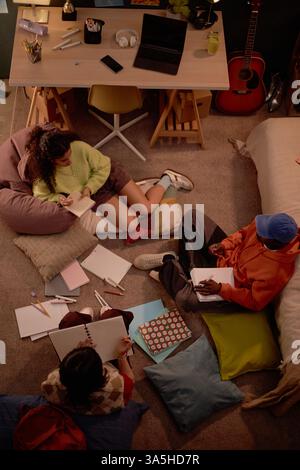 Group of students studying with notes and books on carpeted floor in cozy room with guitar and desk in background Stock Photo