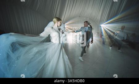 Lida, Belarus - August 25, 2023: Newlywed couple dancing together on their wedding day, surrounded by light rays and guests Stock Photo