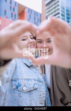 Happy Caucasian friends making a heart shape with hands and smiling outdoors Stock Photo