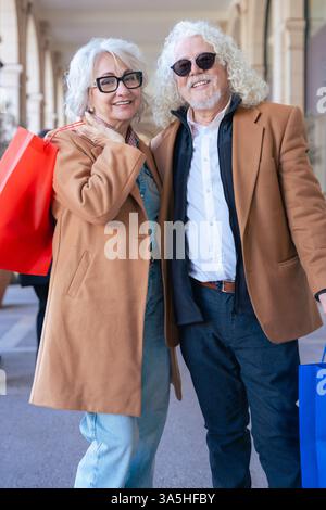 Happy Caucasian senior couple shopping with bags in an elegant urban setting Stock Photo