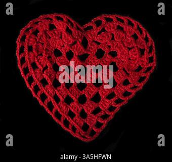 Knitted red heart made of yarn. Black isolated Stock Photo