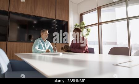 Two multiethnic business partners discussing potential collaboration or joint ventures between companies during negotiation in boardroom. Male profess Stock Photo
