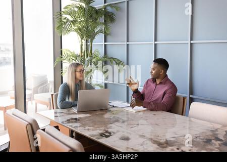 Two multinational teammates talking during meeting in boardroom, working on task, share project details and updates, explore marketing plans, sales st Stock Photo