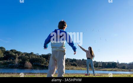 Mother and son enjoying a sunny day by the lake, playing with soap bubbles Stock Photo