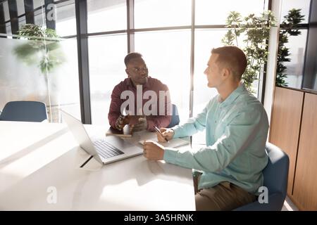 Two multiethnic businessmen, partners discussing terms and conditions of agreement. Manager consulting client, presenting products or services, negoti Stock Photo
