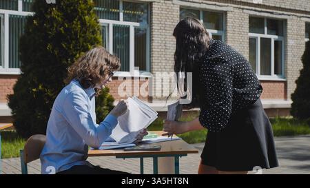 Two students are studying and getting ready for an exam at a desk outdoors near their school Stock Photo